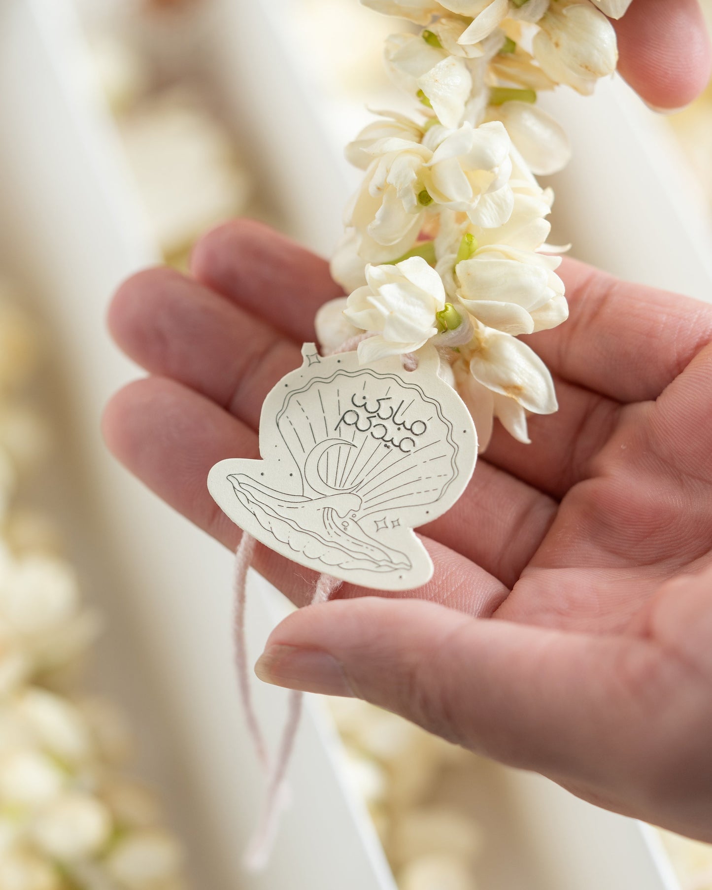 Hand holding a white leaf-shaped object with intricate design against a blurred floral background