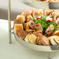 Two-tiered food display with various snacks and salad on a white surface.
