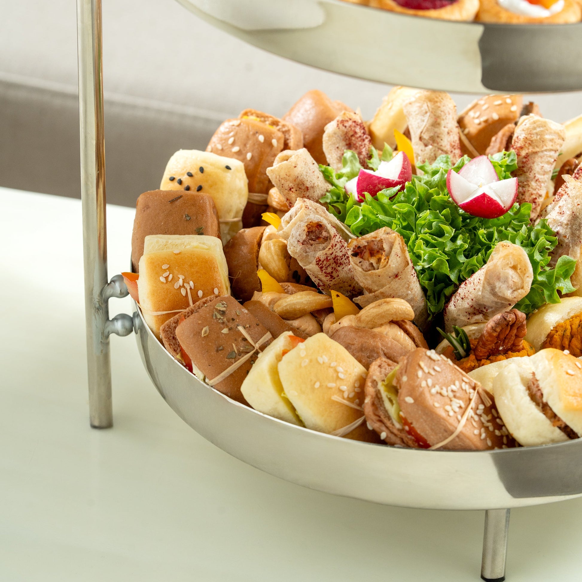 Two-tiered food display with various snacks and salad on a white surface.